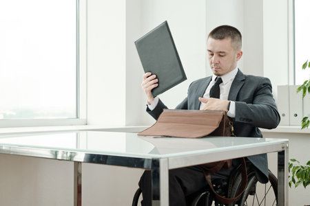Confident boss in formalwear putting folder with documents into briefcase before meeting with partnerの写真素材