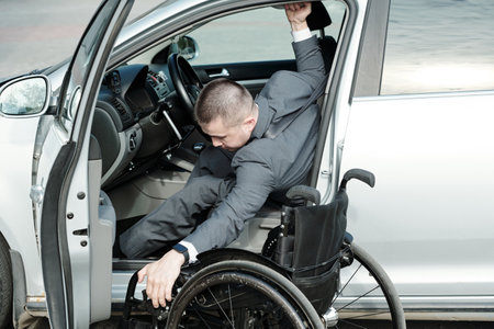 Disabled man taking his wheelchair into car while going home after workの写真素材