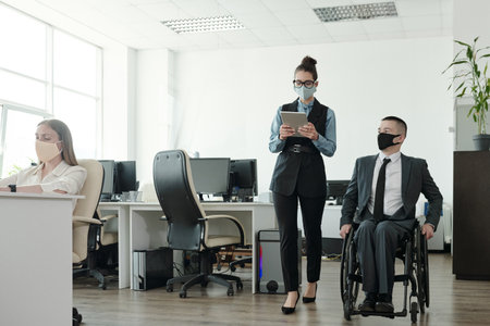 Young businessman and businesswoman in masks and formalwear interacting during workの写真素材