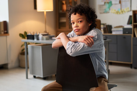African American schoolboy looking at camera after fighting with classmates while sitting in office...