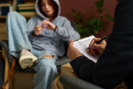 Hands of male school psychologist with pen taking notes in paper document while sitting in front of teenage patientの写真素材