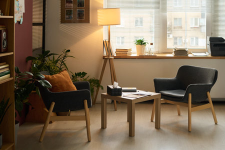 Small square table with box of tissues, paper documents and notepad of psychologist standing between...