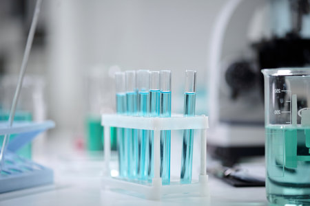 Laboratory equipment with several test tubes filled with a vibrant blue liquid. Beaker in the background along with a pipette can be seen, indicating a scientific experiment settingの写真素材