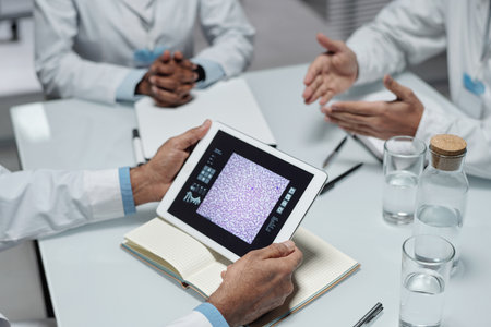 Close-up of healthcare professionals discussing medical results on tablet in modern office environment. Focus on hands and technology reflecting importance of modern devices in medicineの写真素材