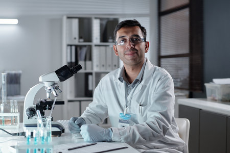 Scientist wearing lab coat and safety glasses examining samples with microscope in modern laboratory setting showing concentration and dedication to scientific researchの写真素材