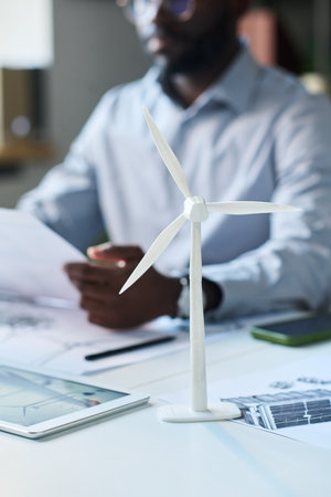 Vertical closeup of plastic wind turbine model on office desk belonging to African American engineer...