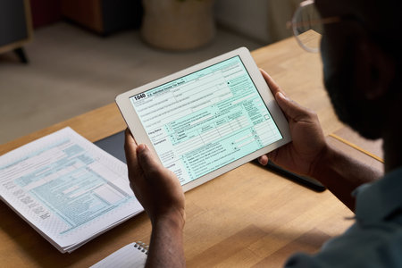 High angle view of unrecognizable Black man holding digital tablet, studying tax document on screen