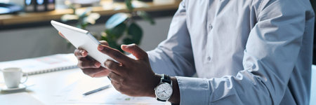 Medium closeup of modern black male manager sitting at desk in office, watching video on digital...