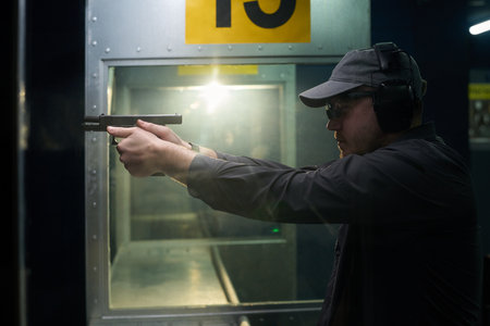 Man wearing protective gear focusing intently while practicing his shooting skills at an indoor...