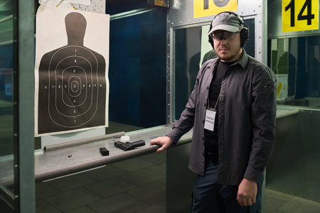 Man practicing shooting at indoor firing range wearing protective gear and serious expression while...