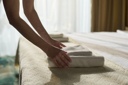 Close-up of hands arranging towels on a neatly made bed in a tastefully decorated hotel room with...