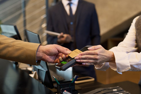 Two people engaging in payment exchange using credit card at reception counter. Focus on hands and card, with blurred background of suited individualの写真素材