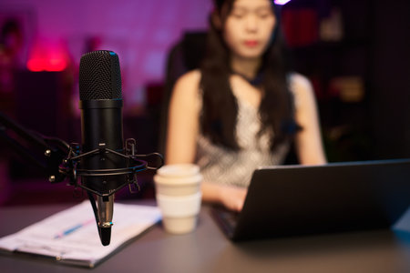 Woman recording podcast using professional microphone setup and laptop, with focus centered on the microphone while she is blurred in the backgroundの写真素材