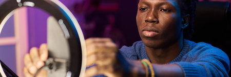 African American male blogger adjusting lighting equipment with smartphone in studio. Man in focus...