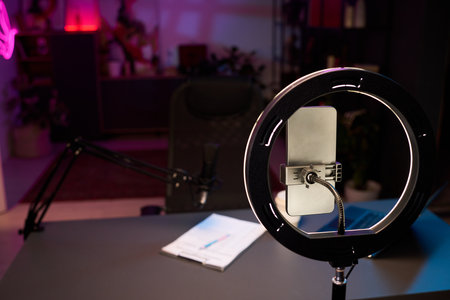 Organized workspace setup including ring light, microphone, smartphone, notes on desk suitable for podcasting or streaming with creative ambiance enhancing atmosphereの写真素材