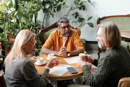 Three colleagues sitting at table enjoying coffee and engaged in discussion surrounded by indoor plants enjoying a relaxed atmosphereの写真素材