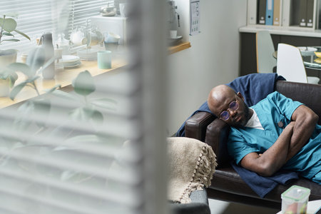 African American senior doctor relaxing in office break room, leaning back on chair with closed...