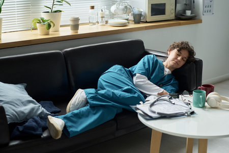 Nursing professional in scrubs taking short rest on sofa in hospital break room Featuring medical...