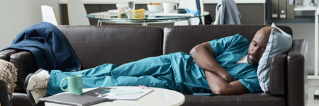African American nurse in scrub suit resting on couch in hospital break room alongside cup on table, showing a moment of relaxation during work shiftの写真素材