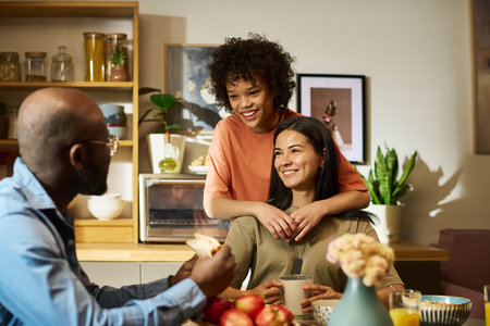 Caucasian middle aged woman sitting at table smiling while Black teenage girl embracing shoulders...