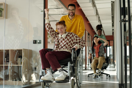 Young adults engaging in coworking space, Caucasian man in wheelchair being pushed by Black man...