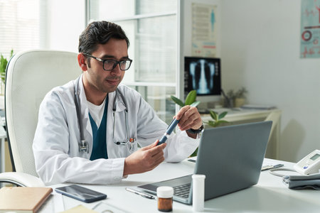 Middle aged Caucasian male doctor sitting at desk examining insulin pen while consulting diabetic...