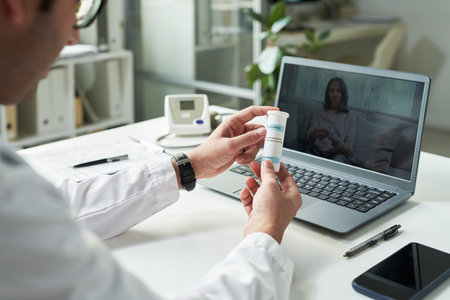 Middle aged Caucasian male doctor holding medication bottle during telemedicine consultation with...