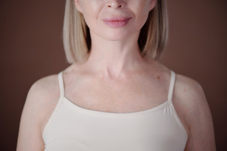 Middle-aged woman with natural blonde hair and fair skin looking straight ahead, wearing sleeveless top in indoor settingの写真素材
