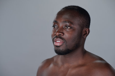 African American man with short hair and beard looking slightly away from camera against grey background, showing contemplative expressionの写真素材