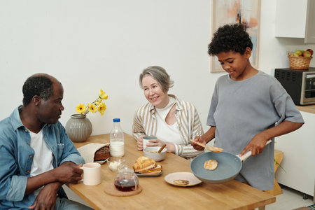 Cheerful family sharing breakfast at wooden table with milk, pancakes, and croissants. Child...