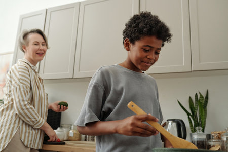 Child stirring ingredients and smiling adult supervising in modern kitchen setting while engaging in culinary activity with joyの写真素材