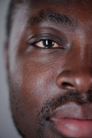 Vertical close-up portrait of African American man gazing into camera, showing half of face with detailed texture and expressions. Capturing intense and focused lookの写真素材
