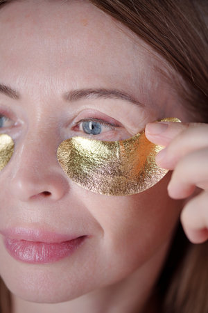 Close-up of Caucasian woman gently applying gold under-eye patches with relaxation and skincare...