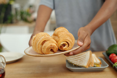 Hands presenting plate with fresh croissants in casual dining setting, accompanied by plate of...