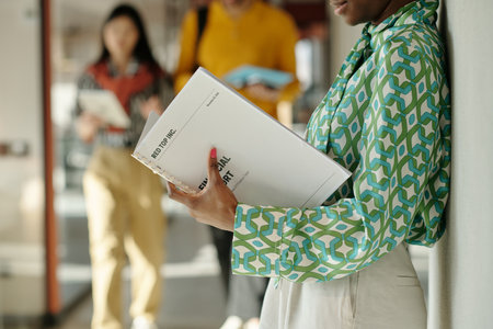 Woman in patterned blouse standing against wall holding business report, two blurred young adult...