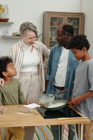 Family enjoying cooking activity together in modern kitchen with various kitchen tools and ingredients on countertopの写真素材