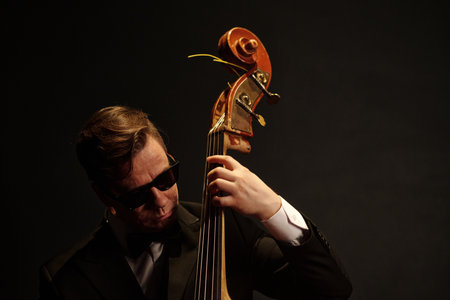 Caucasian man wearing sunglasses playing double bass on stage, focused expression, holding...
