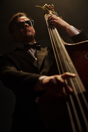 Caucasian middle aged man wearing sunglasses playing double bass on stage, holding instrument...