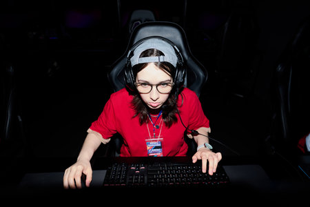 Portrait of Caucasian teenager girl wearing headset sitting at gaming desk playing computer game in esports competition, focused expression, hands on keyboard and mouseの写真素材