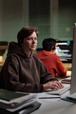 Caucasian woman wearing headset operating computer in scam call center foreground with Asian young...
