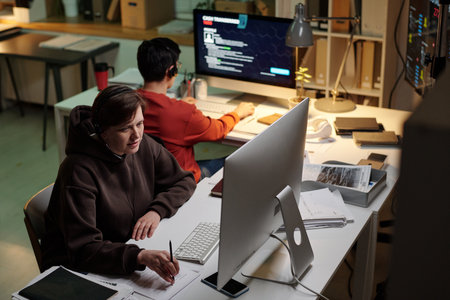 Young adult Asian man and young adult Caucasian woman working at computer desks with headsets,...