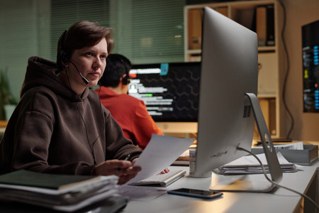 Caucasian young adult woman wearing headset working at computer holding documents in scam call...