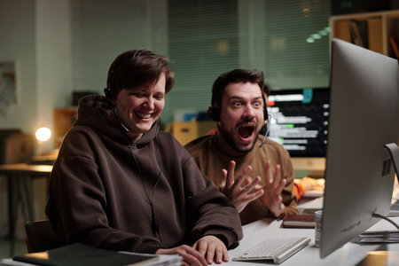 Caucasian woman and man wearing headsets using computer, woman smiling while man reacting with excitement, scam call center environmentの写真素材