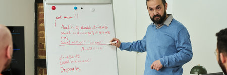 Middle aged Caucasian man teaching programming to group of prisoners, standing by flip chart with...