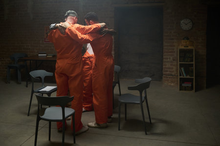 Group of four adult men standing in circle embracing each other in prison visiting room wearing...