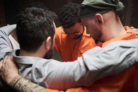 Group of diverse men standing close together in circle embracing shoulders participating in group...