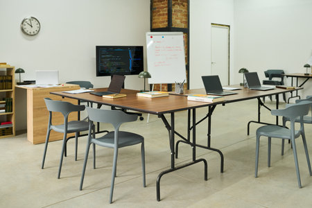 Empty classroom with several laptops, books, and notebooks arranged on tables, whiteboard and monitor displaying educational materials, setting representing prison education environmentの写真素材