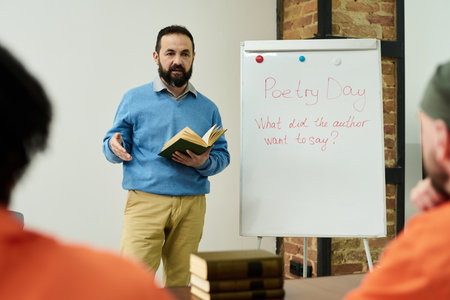 Middle aged Caucasian man standing in front of whiteboard holding book, teaching poetry lesson to...