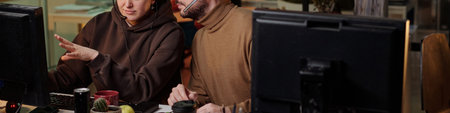 Caucasian woman and man wearing headsets working at computer monitors in office setting, woman gesturing toward screen, man typing on keyboardの写真素材