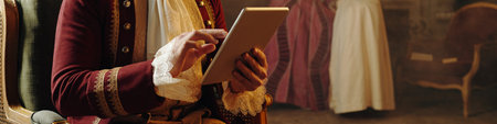 Caucasian middle aged man wearing Baroque style costume using digital tablet while sitting indoors,...